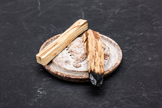 PaPalo Santo aromatic wooden sticks on stone plate on black surface.