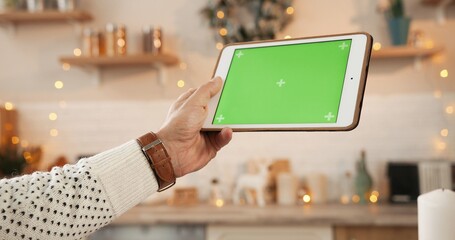Close up shot of male Caucasian young hand holding tablet with green screen with tracking motion at decorated home. Device screen with chroma key in man hands indoors. Technology concept
