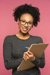 Young happy Afro-American teacher woman isolated on pink studio wall. Student girl wear glasses holding folder, smiling, looking at camera. Education in high school university college concept.