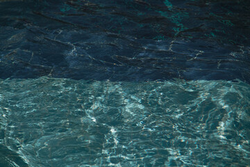 Blue and green pool water. Glare of light in the water. Dark and light symmetry opposition. Water surface frame background.