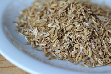 A pile of rice hulls (husks) in close up on a white plate on a wooden table. Husks are a waste...