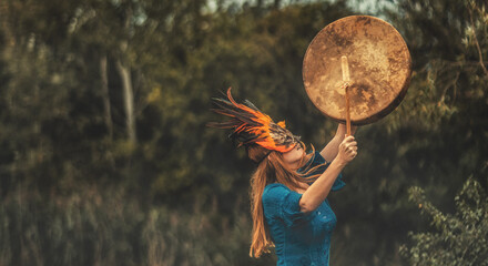 beautiful shamanic girl playing on shaman frame drum in the nature.