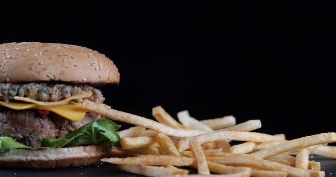 Fast food concept. Falling french fries fried potatoes falling flying on black table near fresh cheeseburger, heavenly delight, appetizing hamburger on dark background close, picture inducing hunger