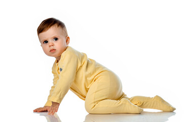 little cute baby girl in a yellow bodysuit tries to crawl on a white studio background.