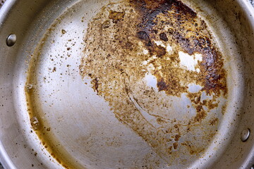 Burnt meat oil and fat remains on the bottom of an iron frying skillet pan close up top view