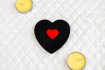 Obraz premium A small red heart is located on a black heart that lies on a white surface next to the candles.