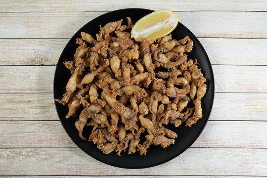 Ration of fried chopitos (squid tips) in black plate on rustic wooden table