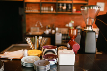 Bar counter with clean dishes close up. Barroom in restaurant, ready for work. Cafe background. Kitchen utensils, cookware (cups, a stack of plates, saucers, spoons, a teapot) on bar in cafe