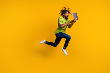 Fototapeta na wymiar Full length photo portrait of excited programmer with dreadlocks jumping up holding laptop in hands isolated on vivid yellow colored background