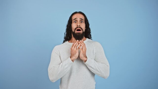 Scaring reaction. Frightened man opening mouth because of being afraid and shaking head in panic, blue studio background
