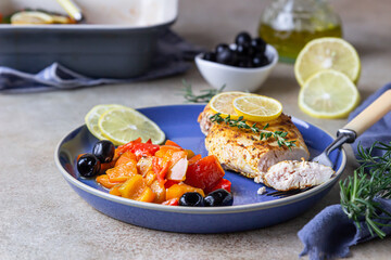 Oven baked or grilled chicken breast with baked bell pepper, lemon and olives, light concrete background. Healthy food.