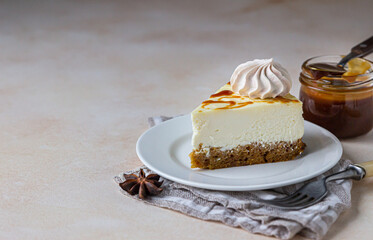 Piece of carrot vanilla cheesecake with salted caramel topping and meringue on a white ceramic plate, light concrete background.