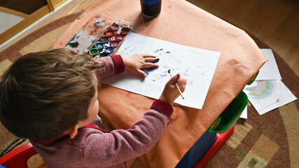 Top view little boy painting with his hands on the sheet of paper. Developing activities at home. Motor skills, creativity, imagination