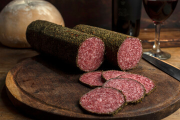 salami, sausages with herbs and cheese cut into slices on wooden board, homemade bread, nuts