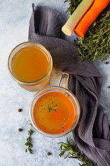 Homemade bone broth in glass mug and vegetables, blue concrete background. Collagen source for the...