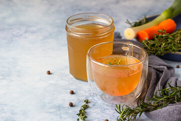 Homemade bone broth in glass mug and vegetables, blue concrete background. Collagen source for the...
