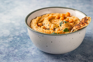 Bowl with homemade hummus garnished with boiled chickpeas, seeds, flatbread and olive oil, blue concrete background. Close up. Selective focus.