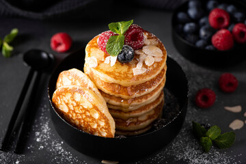 small thin pancakes with fresh berries and honey in a black bowl