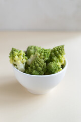 Romanesco cauliflower in a white bowl on a light background. Healthy food concept. Copy space. Vertical orientation.