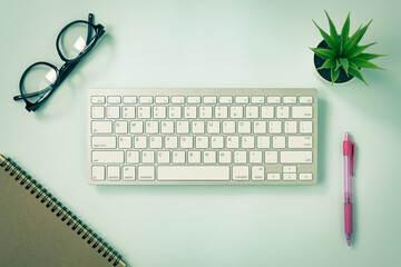 White Portable Computer Keyboard Keys or Keyboard Button and Spiral Notebook and Pink Pen and Office Plant and Glasses on Blue Pastel Minimalist Background in Vintage Tone