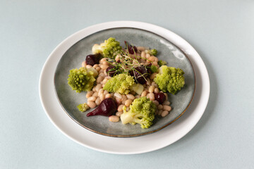 Natural salad of mini beets, romanesco cabbage, white beans and sprouted onion seeds on a gray plate. Healthy nutrition concept. Selective focus. Copy space.