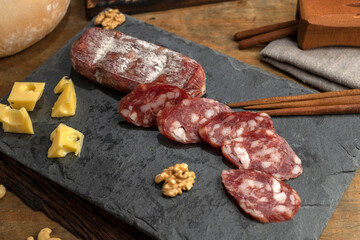 salami, sausages with herbs and cheese cut into slices on wooden board, homemade bread, nuts