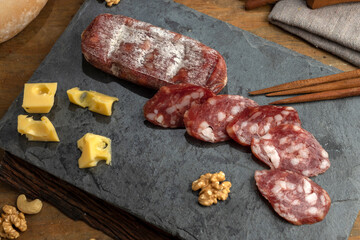 salami, sausages with herbs and cheese cut into slices on wooden board, homemade bread, nuts