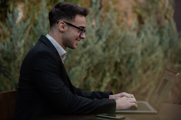 Young successful businessman working on a laptop while sitting in coffee bar during work break lunch. Speaking on his phone while working and drinking coffee.