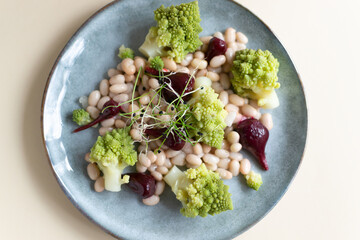 Salad of mini beets, romanesco cabbage, white beans and sprouted onion seeds on a gray plate on a light background. Healthy food concept. Selective focus. Top view.