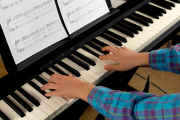 Fototapeta premium A child learns to play the piano in distance learning via a laptop over the Internet