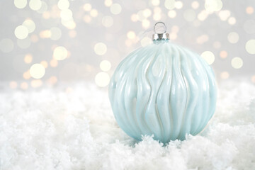 One light blue glass ball for a Christmas tree lies on white snow. Christmas and New Year concept. Bokeh in the background. Close-up