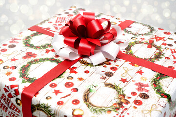 A Christmas gift wrapped in beautiful paper and a red and white bow on a white background. Christmas and New Year concept. Bokeh in the background. Close-up