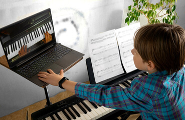Fototapeta na wymiar Boy learning to play the piano in distance learning via laptop over the Internet