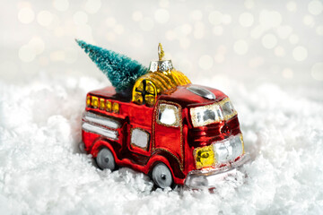 Glass decoration for a Christmas tree on a white background. A red car with a fluffy pine tree stands on the white snow. Bokeh in the background. Close-up