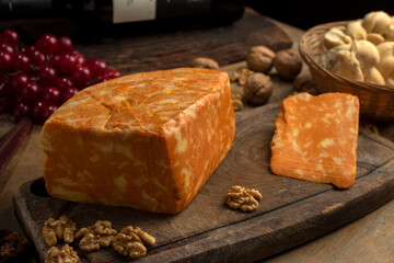artisan cheeses with dried fruits glass of wine, homemade country bread, bunch of grapes, on wooden board with knife