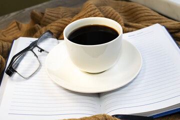 On an open Notepad with lines is a Cup of coffee and glasses for vision. Warm brown sweater. Concept of leisure and comfort