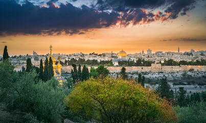 Fototapeta premium Beautiful dramatic autumn sunset over the Old City Jerusalem, with the Dome of the Rock, the Golden Gate and the Russian Orthodox church of Mary Magdalene seen through fall trees on Mount of Olives