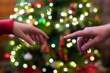 Man and woman two hands reaching for each other on the christmas tree background with glowing bulbs. Close up