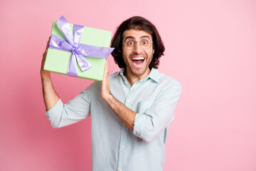 Photo of cheerful funny brown hair guy holding gift wear spectacles shirt isolated on pastel pink color background