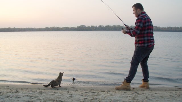 Male Angler Catching Fish Near Cat In Morning