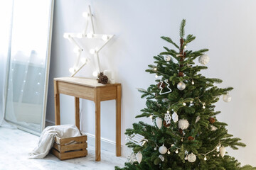 Christmas tree in a white room. Star shaped lamp on a wooden table on the background