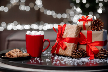 Hot coffee mug with sweets, gifts and pine cones on the table, gold background with white garlands