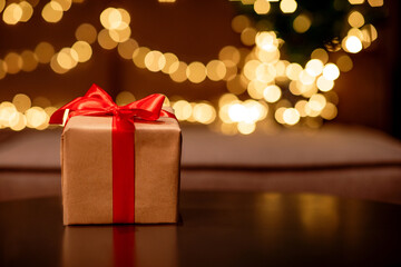 Gift box with a red bow on a brown table with flickering lights bokeh background.
