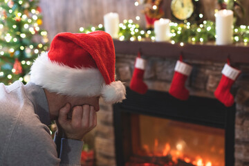 Sad man in Santa Claus hat in a depression feeling negative emotions during christmas celebrations