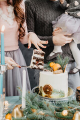 Young family with a daughter in festive outfits at a served table with candles, garlands, sparklers and a cake near the Christmas tree on New Years Eve
