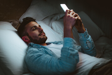Young man using smart phone mobile - Millennial guy with cellphone lying on bed at home -...