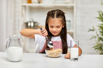 smiling cute little girl eating breakfast: cereal with the milk in the kitchen. healthy breakfast