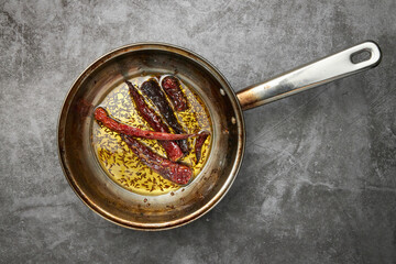 Dried red chillies in a steel pan with oil and cumin seeds - Powered by Adobe