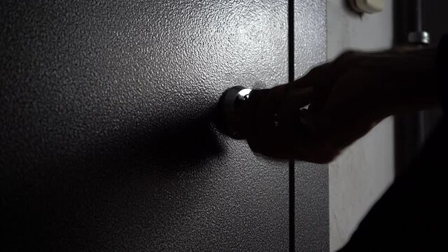 Close the door quickly with the key. The man's hand hastily inserts the key into the door lock and closes the front metal door. Close-up of keys and hand.