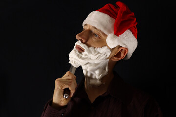 Bad Santa with a beard of shaving foam shaves with a knife on a black background